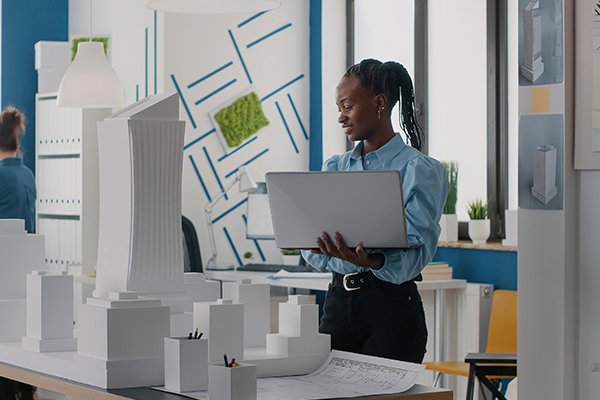 A student holding a laptop whilst looking at a physical prototype of a developed estate