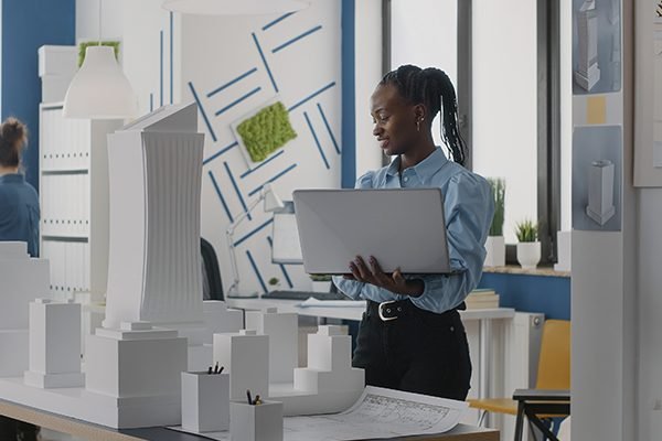 A student holding a laptop whilst looking at a physical prototype of a developed estate