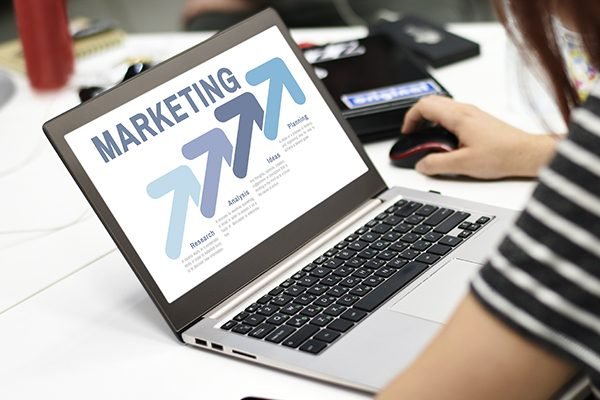 A woman in front of a laptop with a screen that reads Marketing